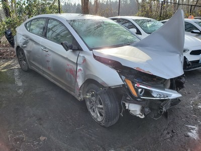 Damaged silver sedan with a crumpled front end and visible scratches, parked among intact vehicles. Illustrates the aftermath of a collision.