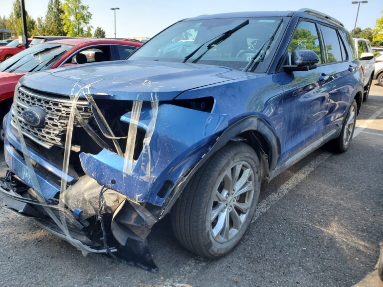 Damaged blue Ford Explorer parked in a lot, showing a crumpled front end secured with tape. Relevant for discussions on car accidents or repairs.
